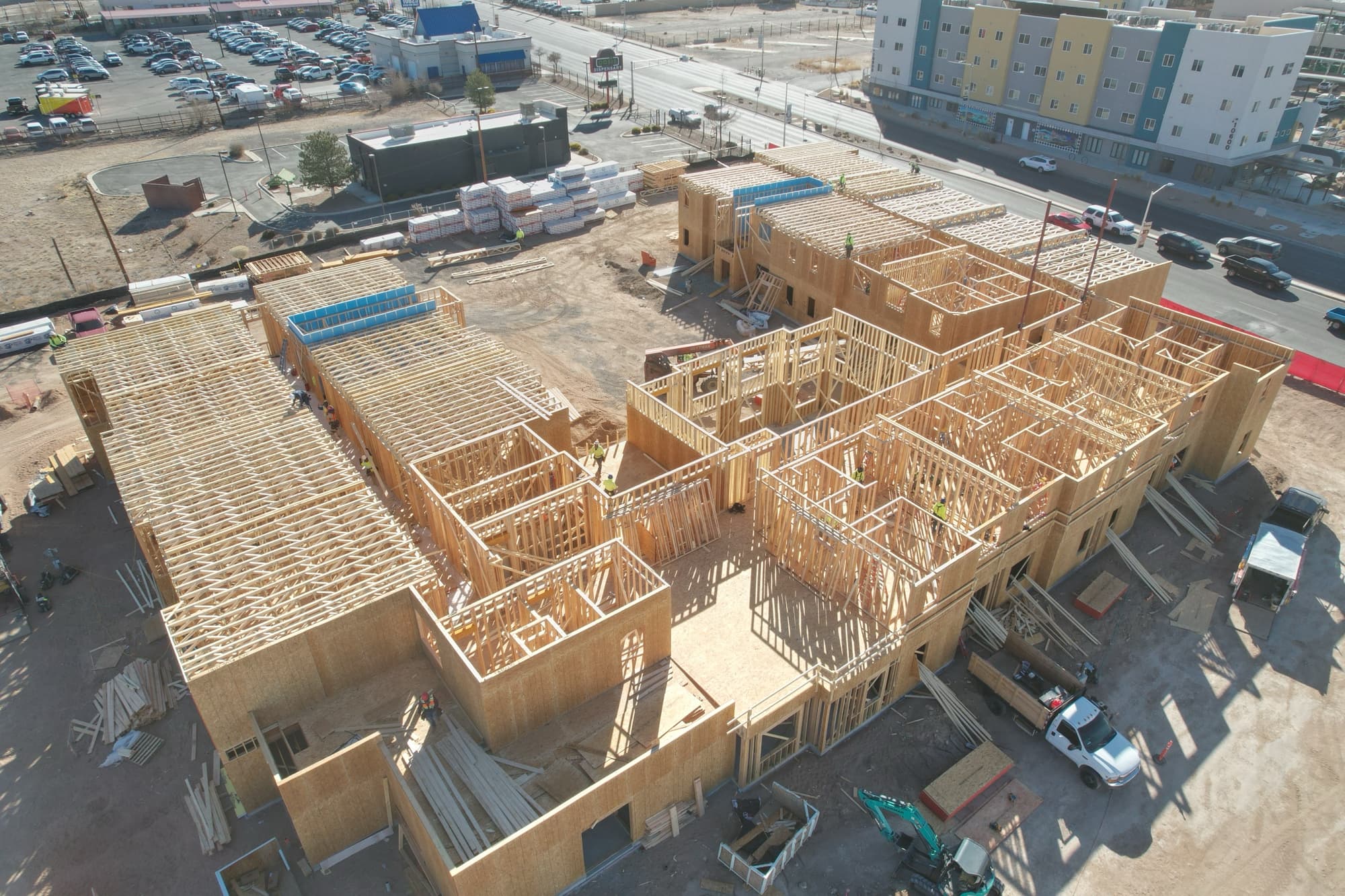 apartment construction showing second floor of wood framing, construction site and 4 story apartment building in background.